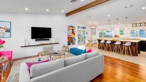 Een moderne woonkamer met een flatscreen televisie, een bank, een salontafel en een keuken met barstoelen.
