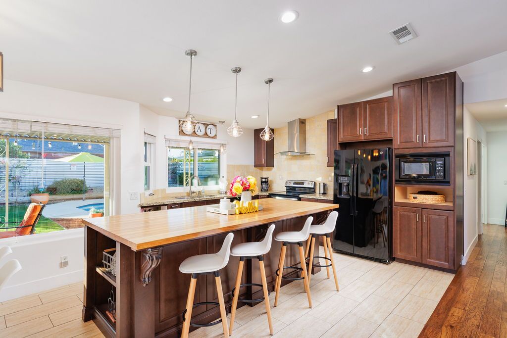 A modern kitchen with a central island, bar stools, wooden cabinets, and a view of the backyard.