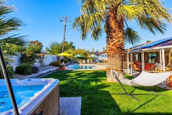 Un patio trasero con piscina, hamaca y mobiliario exterior.