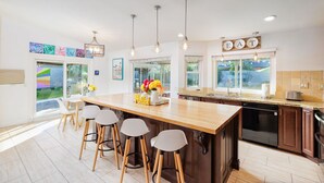 Een moderne keuken met een centraal kookeiland, barkrukken, hanglampen en uitzicht op de omgeving.
