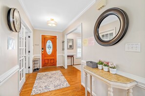 A hallway with a wooden floor, a white door, a mirror, and a console table with potted plants.