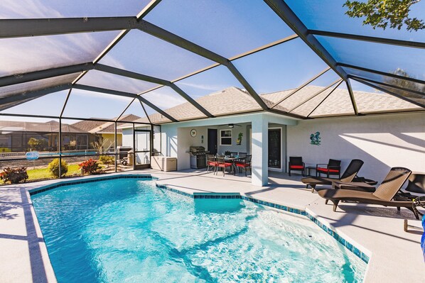 A swimming pool with a glass enclosure, outdoor seating, and a patio area.