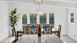 Ein Essbereich mit einem Marmortisch, Holzsesseln, einer Chandelüster und großen Fenstern.