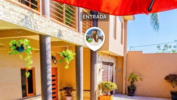 Zona de piscina con una toldo rojo, plantas en macetas y un letrero que dice 'ENTRADA'.