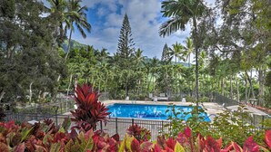 A swimming pool surrounded by lush greenery and palm trees, with a clear sky above. - King size Bed, 1BR condo, Makaha Valley, with Mtn and Ocean views (Waianae)