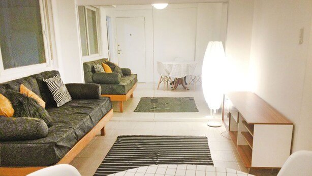 A living room with a sofa, a coffee table, and a lamp. - Piso céntrico y funcional con excelente ubicación. (ABQ)