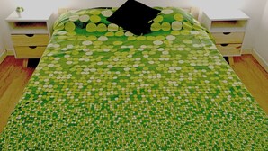 A bed with a green and white polka dot bedspread, two bedside tables with drawers, and a white wall. - Piso céntrico y funcional con excelente ubicación. (ABQ)