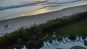 Blick auf einen Strand mit Wellen, einem Sonnenuntergang und einem Poolbereich mit Liegestühlen.