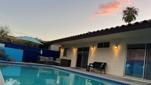 Ein Pool mit Fliesenbord, eine Terrasse mit Gartenmöbeln und ein Haus mit einem geFliesenen Dach und Fenstern.
