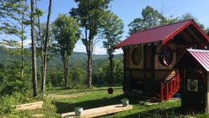 A cabin with a red roof, surrounded by trees and a grassy area.