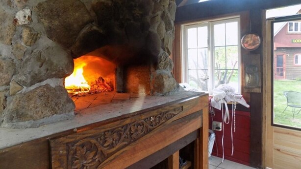 A stone fireplace with a fire burning inside, a wooden table with carved details, and a view of the outside through a window.
