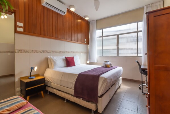 A hotel room with a bed, bedside table, lamp, and a window with blinds. - 5 Minutes From Copacabana Beach Stc905 (Rio de Janeiro)