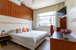 A hotel room with a bed, a desk, a TV, and a window with a view of buildings. - 5 Minutes From Copacabana Beach Stc905 (Rio de Janeiro)