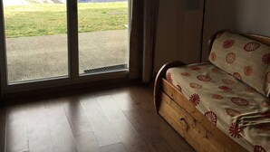 Una habitación con sofá de madera, una lámpara de pie y vistas a las montañas a través de grandes ventanales.