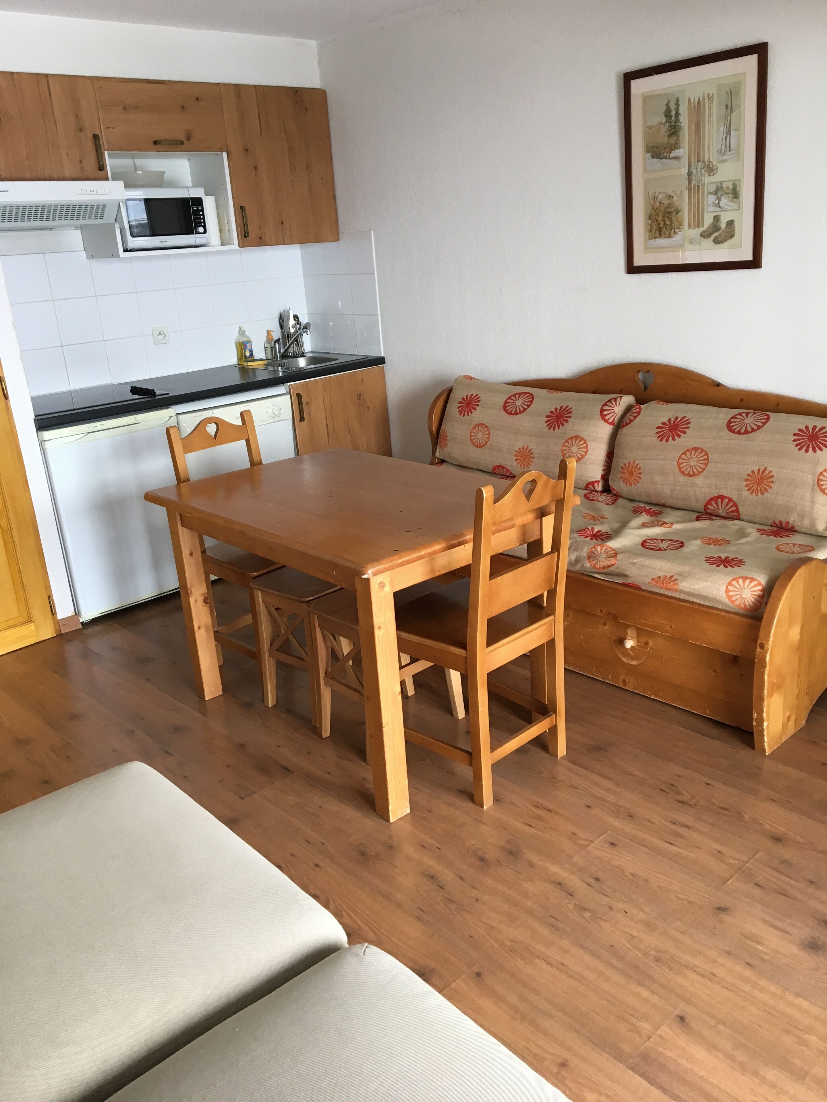 Un espacio habitable compacto con una mesa y sillas de madera, un sofá con cojines estampados, un microondas y una pequeña kitchenette.