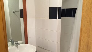 Un baño con lavamanos blanco, tocador de madera y zona de ducha.