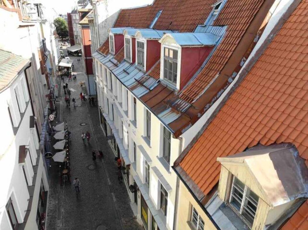 Une rue étroite, bordée de bâtiments des deux côtés, avec des toits recouverts de tuiles rouges et un pavé.