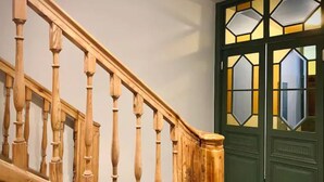 Una escalera de madera con una puerta verde y vidrieras geométricas.