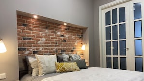 Un dormitorio con cabecera de ladrillo, cama con ropa de cama a rayas y una mesita de noche con cajones.