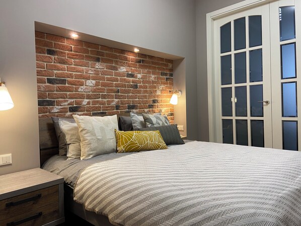 Un dormitorio con cabecera de ladrillo, cama con ropa de cama a rayas y una mesita de noche con cajones.