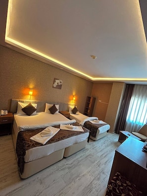 A hotel room with two beds, a desk, a chair, and a large window with curtains.