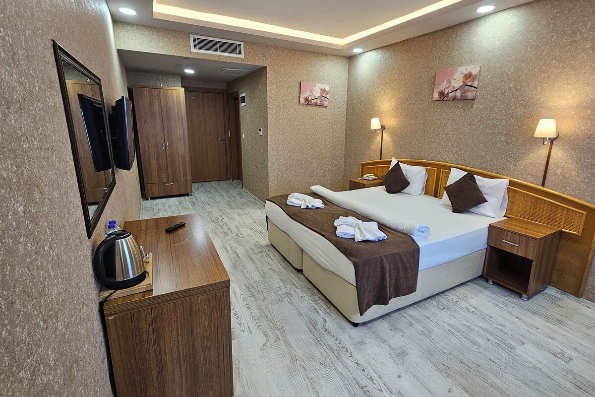 A hotel room with a bed, bedside tables, a TV, and a wardrobe.