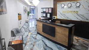 A reception area with a marble floor, a wooden reception desk, framed certificates, and a wall clock displaying Tokyo, Trabzon, and Londra times. - Pointbreak Hotel (Trabzon)