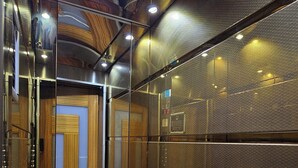An elevator interior with metallic walls, a textured ceiling, and a door with wooden paneling. - Pointbreak Hotel (Trabzon)