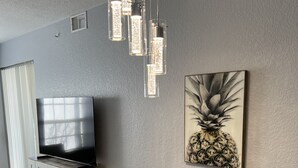 En moderne stue med et fladskærms-TV, et spisebord med stole, en dekorativ ananas-kunst og et unikt pendelarmatur.
