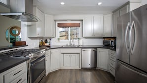 A modern kitchen with white cabinets, stainless steel appliances, and a window with a brown valance. - Amazing Views with Heated Pool and Jacuzzi Near Beach (Solana Beach)