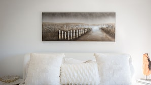 A bedroom with a large bed, two white pillows, a white textured throw, and a painting of a pathway on the wall. - Amazing Views with Heated Pool and Jacuzzi Near Beach (Solana Beach)