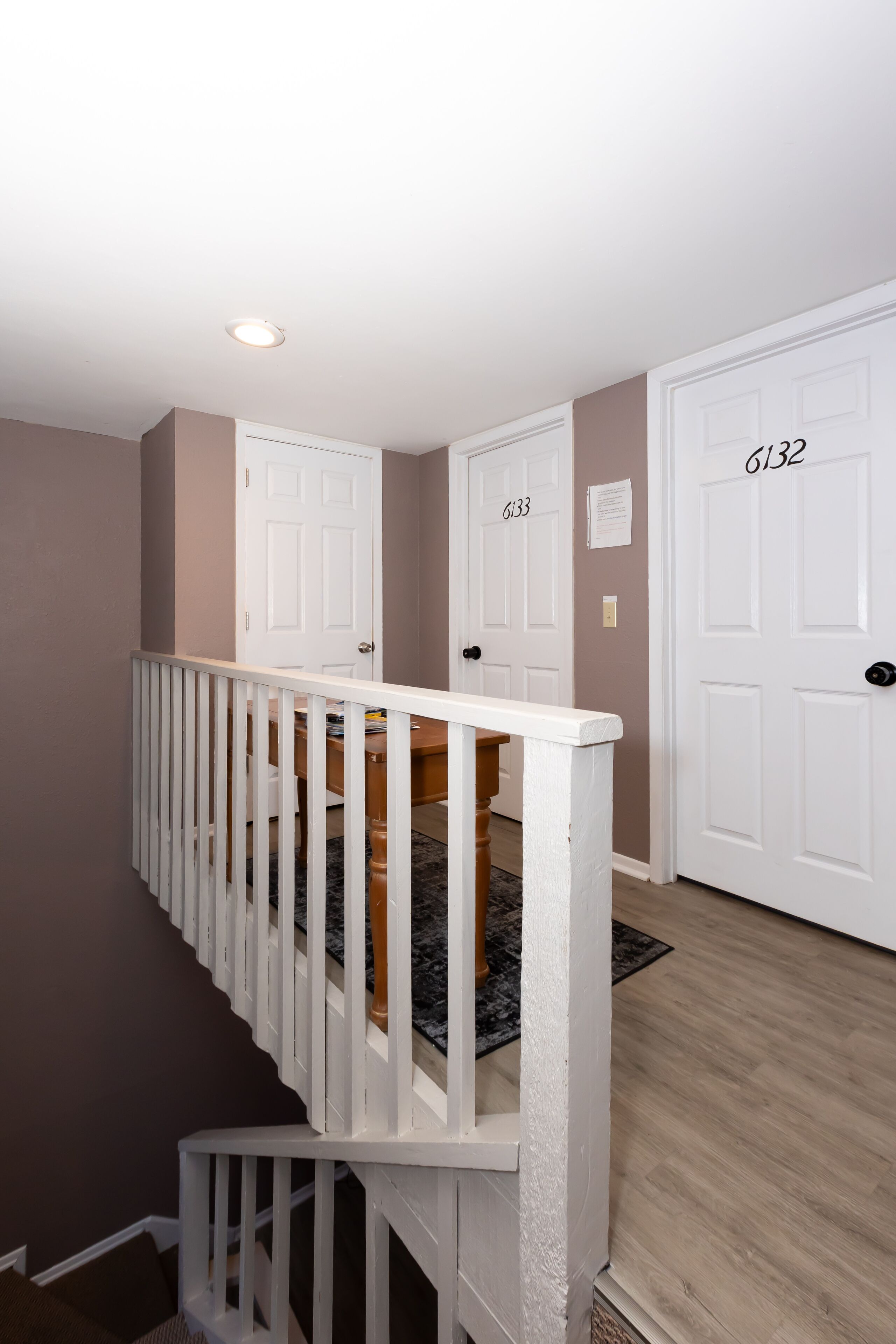 A staircase with white railings leading to a landing with three white doors labeled 6132, 6133, and 6134.