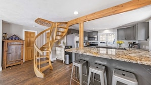 Una cocina con una escalera espiral de madera, una isla de mármol y taburetes de bar.