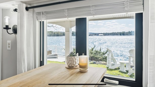 Una habitación con una mesa de madera, un vaso con una bebida y vistas a un lago a través de amplios ventanales.