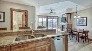 A spacious kitchen with granite countertops, a dishwasher, wooden cabinets, a dining area with a table and chairs, a stone fireplace, and a large window offering a view. - Peak 7 Ski In Ski Out, 1 bedroom condo Breckenridge. Next to the Super Chair (breckenridge)