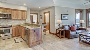 A spacious kitchen with wooden cabinets, a built-in island, and stainless steel appliances. There is a living area with a leather sofa and a coffee table. - Peak 7 Ski In Ski Out, 1 bedroom condo Breckenridge. Next to the Super Chair (breckenridge)