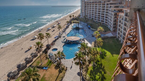 Un resort con playa, varias piscinas y un gran edificio de hotel.