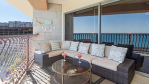 Un balcón con un sofá de mimbre, una mesa de vidrio con bebidas y vista al mar.