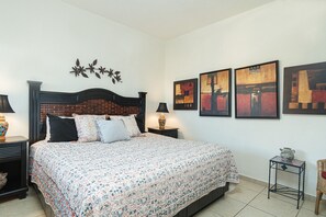 A bedroom with a bed, two nightstands, a wall-mounted lamp, and three framed artworks.