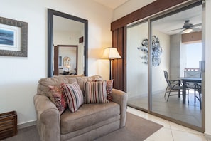 A living room with a sofa, pillows, a lamp, and a sliding glass door leading to a dining area.