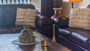 Un salón acogedor con un sofá de cuero, una mesita con un jarrón decorativo y vasos de whisky, y una lámpara que ofrece una luz cálida.