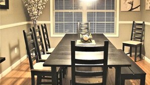 A dining room with a long table, six chairs, a chandelier, and a window with blinds.