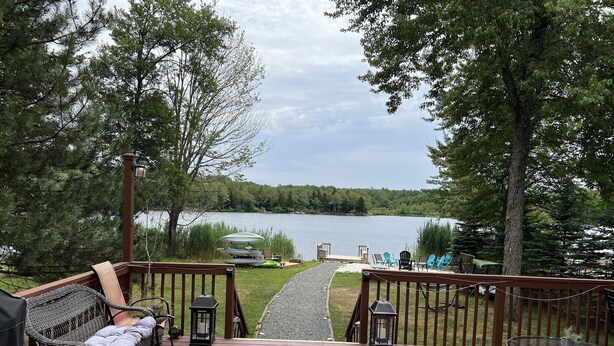 A wooden deck with outdoor furniture, a glass table, and a view of a lake.