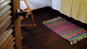 Un dormitorio con cabecera de madera, cama con ropa blanca, alfombra a rayas colorida y una mecedora de madera.