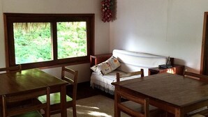 Una habitación con una mesa y sillas de madera, un sofá con un cojín estampado y una ventana con vistas a la vegetación.