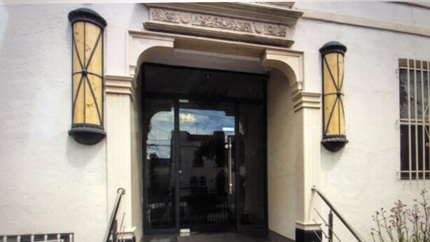 A building entrance with a black door, a set of stairs, and two wall-mounted lanterns.