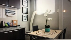A small kitchen with dark cabinets, a countertop with a kettle, a box, and a plant on the table.