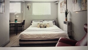A bedroom with a bed, a desk, a chair, and a window.