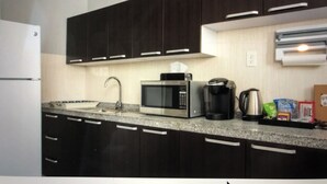 A kitchen with dark cabinets, a microwave, a coffee maker, and a refrigerator.
