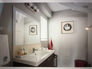 A modern bathroom with a large mirror, a white sink, and two framed pictures on the wall. - Modern studio apartment in Koreatown (Los Angeles)